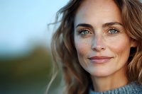 Confident middle-aged Caucasian woman with freckles and green eyes smiling outdoors in natural light wearing casual sweater, displaying genuine happiness and contentment.