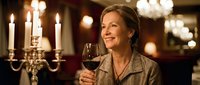 Elegant mature woman enjoying red wine in upscale restaurant with candlelight and chandeliers creating romantic dining atmosphere for special occasion celebration.