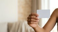 Young adult with medium brown skin tone holding blank white card in hand, suitable for business card mockups, promotional materials, and marketing campaigns.