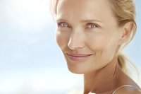 Close-up portrait of smiling blonde Caucasian woman with natural makeup and glowing skin against soft light background for beauty and skincare concepts.