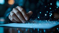 Magical glowing particles float above digital tablet screen as person interacts with device in dark room with blue ambient lighting and bokeh effects.
