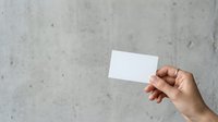 Hand holding blank white business card against concrete wall background for branding and corporate identity mockup presentations.