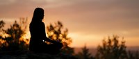 Woman silhouette meditating in lotus pose during golden sunset with trees in background. Peaceful mindfulness and yoga practice for wellness and relaxation.