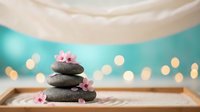Zen spa stones balanced with pink cherry blossoms on bamboo mat, soft bokeh lights creating peaceful wellness atmosphere for meditation and relaxation.
