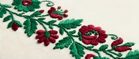Traditional folk embroidery border with red flowers and green leaves on cream linen fabric, showcasing handcraft textile art and ethnic decoration.