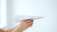 Close-up of a hand holding a white paper airplane against a bright, blurred background, symbolizing innovation, ideas, and new beginnings.