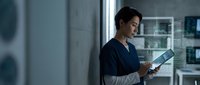 Asian female healthcare professional reading medical chart in modern hospital corridor during night shift work.