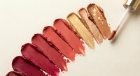 Colorful lipstick swatches in warm tones from deep burgundy to golden shimmer displayed on neutral background for cosmetic marketing.