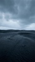 Dramatic stormy sky over windswept sand dunes with rippled patterns and footprints creating moody desert landscape for environmental and travel concepts.
