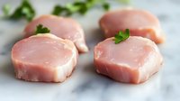 Raw pork medallions with fresh parsley garnish on marble surface, close-up view showing meat texture and marbling for culinary and food photography.