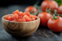 Fresh diced tomatoes in wooden bowl with whole ripe tomatoes on dark rustic wooden background, selective focus on chopped vegetables.