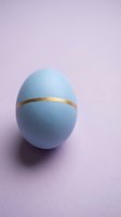 Blue Easter egg with gold band on pastel purple background for spring holiday celebration and festive decoration projects.