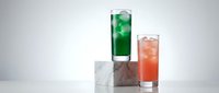 Refreshing colorful cocktails with ice cubes on modern white surface. Green and orange drinks in tall glasses for summer party and beverage menu design.