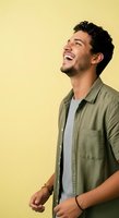 Young man with dark curly hair and olive skin tone, wearing olive button-up shirt over gray t-shirt, smiling joyfully against yellow background. Suitable for lifestyle, happiness, and portrait projects.