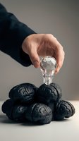 Business hand placing crystal light bulb on pile of black brain models representing innovation, creativity and intellectual property concepts.