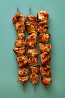Grilled chicken kebabs with green bell peppers on metal skewers against turquoise background. Marinated meat pieces show appetizing char marks and glazed coating.