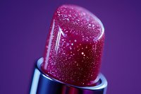 Macro shot of pink lipstick with glitter particles and sparkles on purple background, showing luxury cosmetic texture and shimmer detail for beauty and makeup advertising.