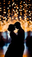 Romantic silhouette of couple dancing with magical bokeh lights in warm golden tones creating dreamy atmosphere at wedding reception or celebration event.
