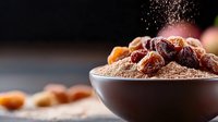 Dried dates and date sugar powder in ceramic bowl on dark background with flying sugar particles, healthy natural sweetener for cooking and baking.