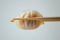 Asian steamed dumpling held by wooden chopsticks against light background, showing delicate pleated texture and spicy seasoning details.