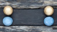 Decorative composition with golden and light blue spheres arranged symmetrically on dark wooden background, creating minimalist modern design pattern.