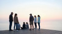 Family group standing together on wooden pier at sunset, enjoying peaceful waterfront moment during golden hour.
