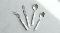 Elegant flatlay of stainless steel cutlery with white handles arranged on neutral background, suitable for dining, restaurant, and tableware design projects.