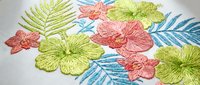 Colorful tropical embroidery with hibiscus flowers and palm leaves in coral, lime green and turquoise thread on white fabric for summer fashion and decor.