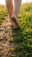 Barefoot runner jogging on dirt trail through green grass field during golden hour, close-up of female legs in motion for outdoor fitness and wellness.