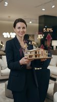 Real estate agent holding wooden house model with growth percentage arrows in modern office interior, displaying property investment and market increase.