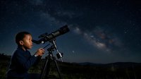 Young boy with medium skin tone gazing through telescope at starry night sky with milky way visible, outdoor astronomy and education concept for science learning and exploration.