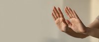 Two open hands raised with palms facing forward against a neutral beige background, conveying prayer, supplication, or peaceful gesture.