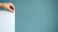 Caucasian hand holding blank white paper sheet against teal background, suitable for advertising, marketing campaigns, presentations, and promotional materials.