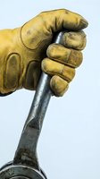 Gloved hand gripping a metal wrench, close-up of a worker in yellow leather safety glove holding a tool for repair and maintenance.