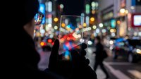 Hand holding transparent smartphone with city lights bokeh background at night creating futuristic technology concept for mobile apps and digital communication.