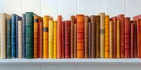 Colorful vintage hardcover books arranged in rainbow order on white wooden shelf, spines showing varied heights and textures creating harmonious literary display.