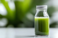 Fresh green smoothie or juice in glass bottle with metal lid on white surface against blurred natural background, healthy detox drink concept.