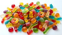 Colorful assorted gummy candies including bears, worms, rings and fruit shapes scattered on white background. Sweet treats for confectionery displays.