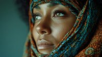 Young African woman with colorful traditional headwrap looking upward with hope and determination against teal background for cultural diversity projects.