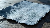 Dark gray slate stone piece with rough natural texture and torn edges on wooden surface for rustic kitchen design and food presentation backgrounds.