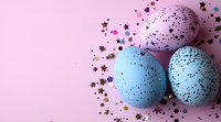 Festive Easter eggs in pastel pink and blue tones decorated with golden star confetti on pink background. Creative holiday composition with copy space.