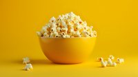 Fresh popcorn served in bright yellow ceramic bowl against vibrant yellow background with scattered kernels, minimalist food photography composition.