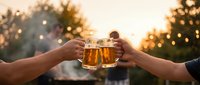 Two hands toasting with beer mugs at sunset creating warm golden hour atmosphere for celebration and friendship moments.
