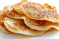Freshly baked crispy flatbread sprinkled with sesame seeds and spices on white background, macro shot showing detailed texture and golden-brown crust.