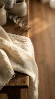 Natural linen fabric draped over rustic wooden surface with ceramic pottery in warm sunlit artisan workshop creating cozy handmade craft atmosphere.