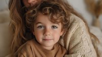 Loving mother embracing her adorable curly-haired toddler son in cozy home setting. Warm family bonding moment with soft natural lighting and neutral tones.