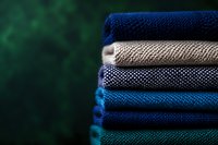 Stack of folded knitted sweaters in blue and beige colors on dark green background. Cozy winter clothing collection for seasonal wardrobe and fashion concepts.