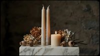 Cream taper candles and pillar candle arranged with dried flowers on marble block against dark textured background for home decor and event styling.