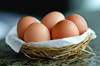 Fresh brown eggs nestled in straw-lined basket with white cloth, captured in soft natural lighting against blurred background, showcasing organic farm produce.
