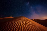 Majestic sand dunes under starry night sky, rippled desert landscape illuminated by moonlight with purple and orange cosmic horizon creating dramatic natural scenery.